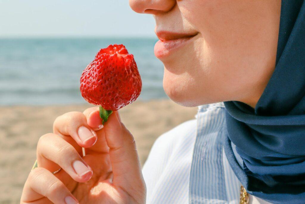 Close-up of a woman savoring a strawberry on a sunny beach day.